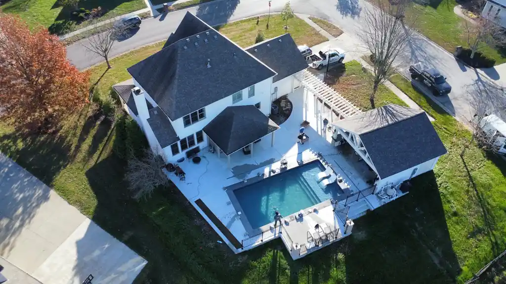 Drone view of a white house with its pool and patio in a subdivision