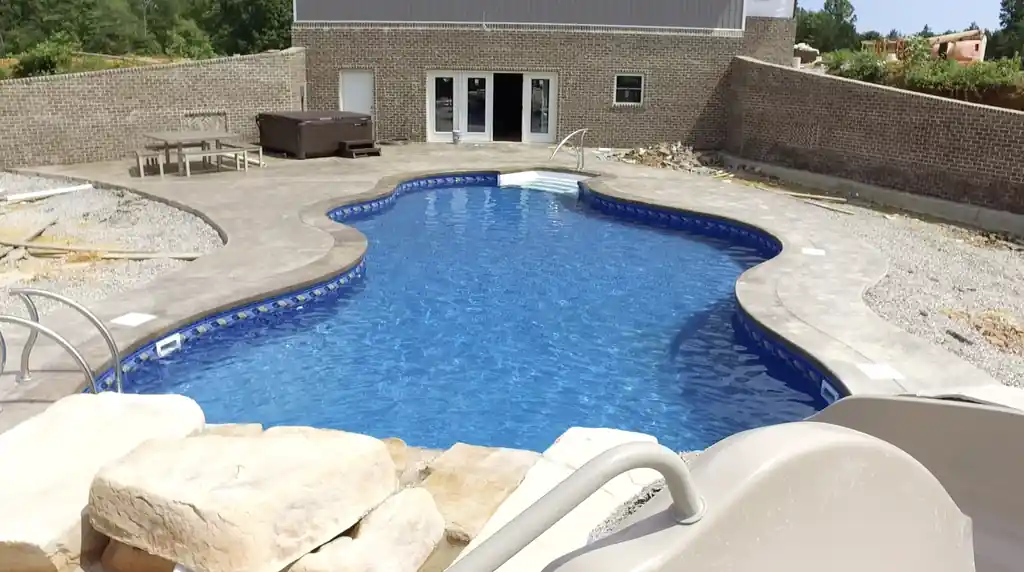 Freeform vinyl pool mid-build, boulders set and slide in place before the deck is finished