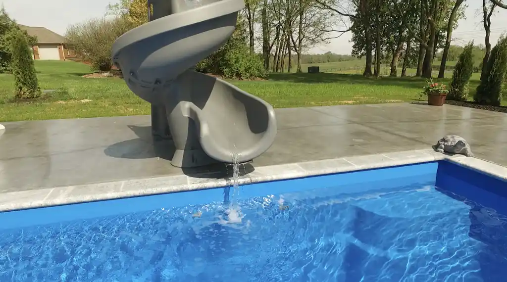 Spiral slide running into a deep blue pool on a wet concrete deck