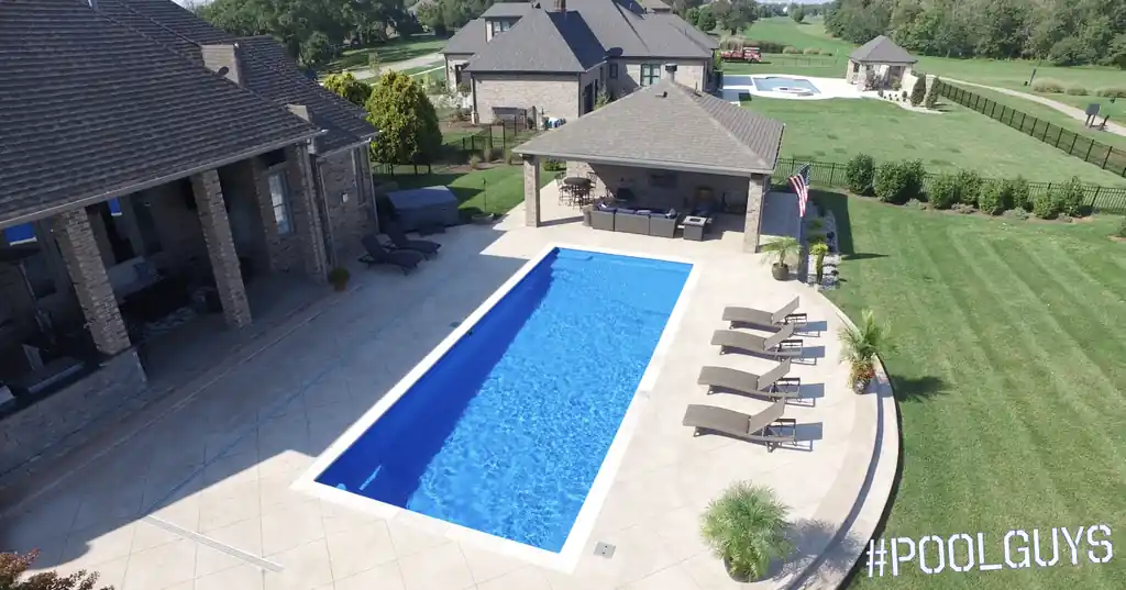 Drone view of a long rectangular pool beside a covered pavilion and lounge chairs