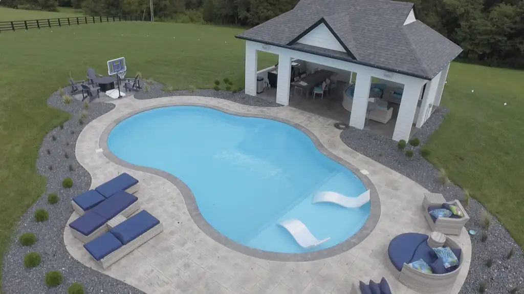 Lake-shaped pool with a grey paver border, navy lounges and a white pool house