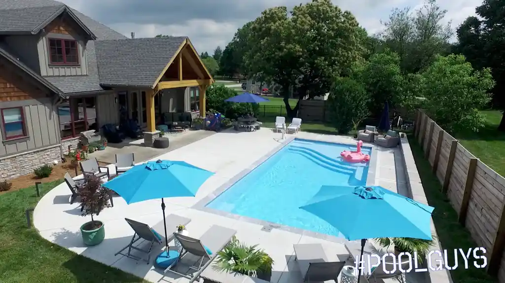 Pool with entry steps, blue umbrellas and a wood privacy fence