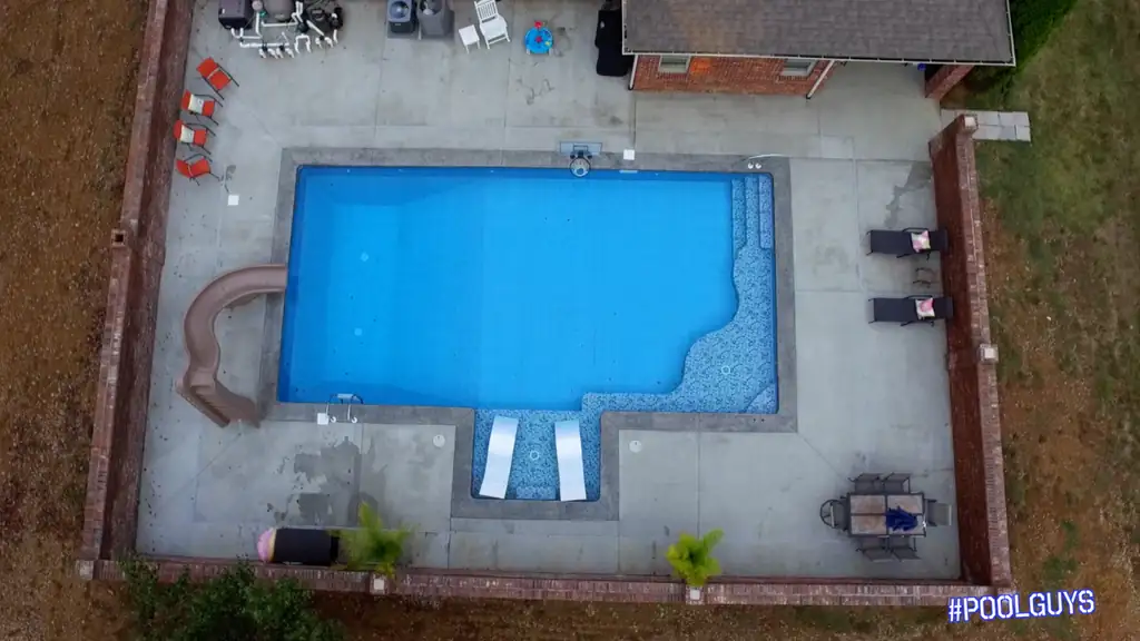 Straight-down view of a pool with a slide and sun-shelf loungers inside brick walls