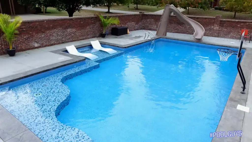 Mosaic-tiled tanning ledge with loungers, a slide and a basketball hoop on the deck