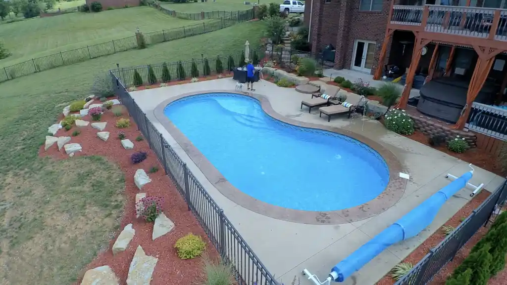 Kidney-shaped pool behind a black aluminium fence with a stone-edged garden