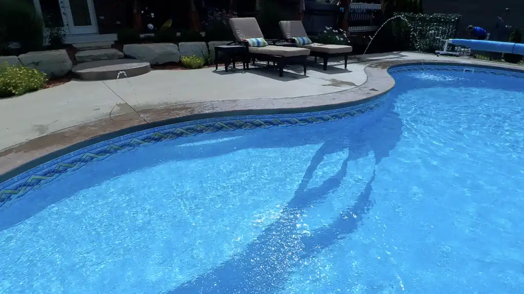 Freeform pool with deck jets, loungers and boulder landscaping along the coping