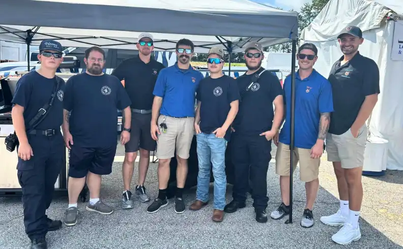 Eight members of the American Pool & Spa crew in navy and blue polos under an event tent